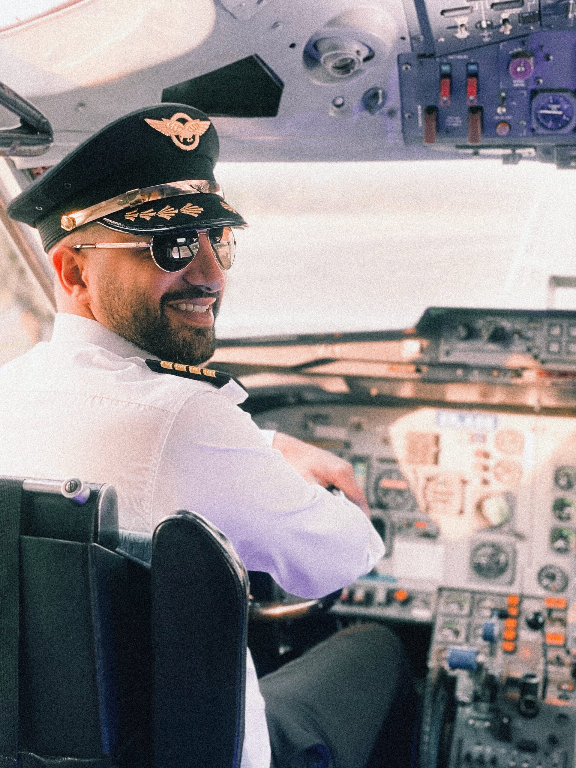 A pilot with sunglasses in the flight deck turns and smiles at the camera